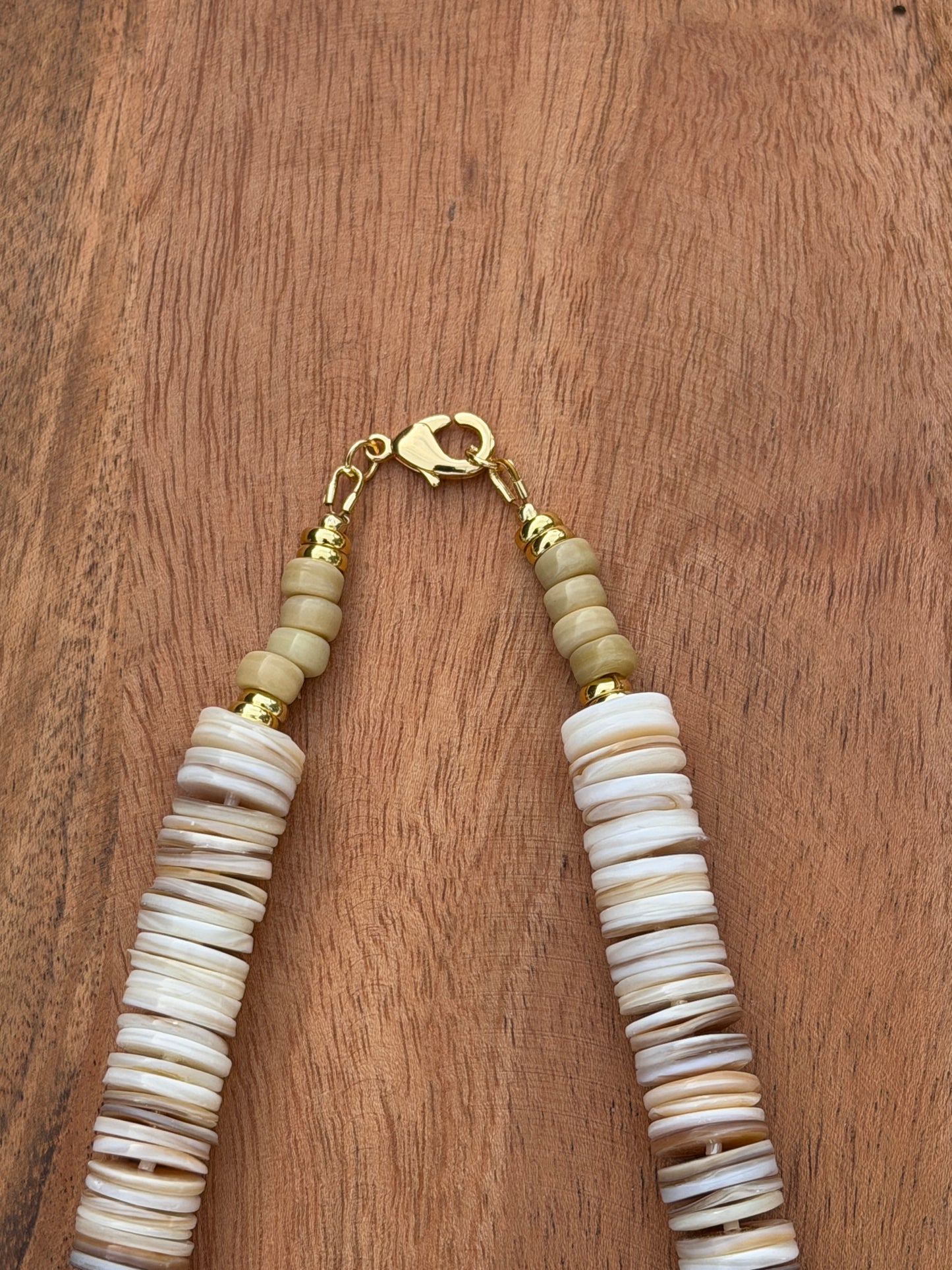 Necklace with shell beads and gold clasp on a wooden surface