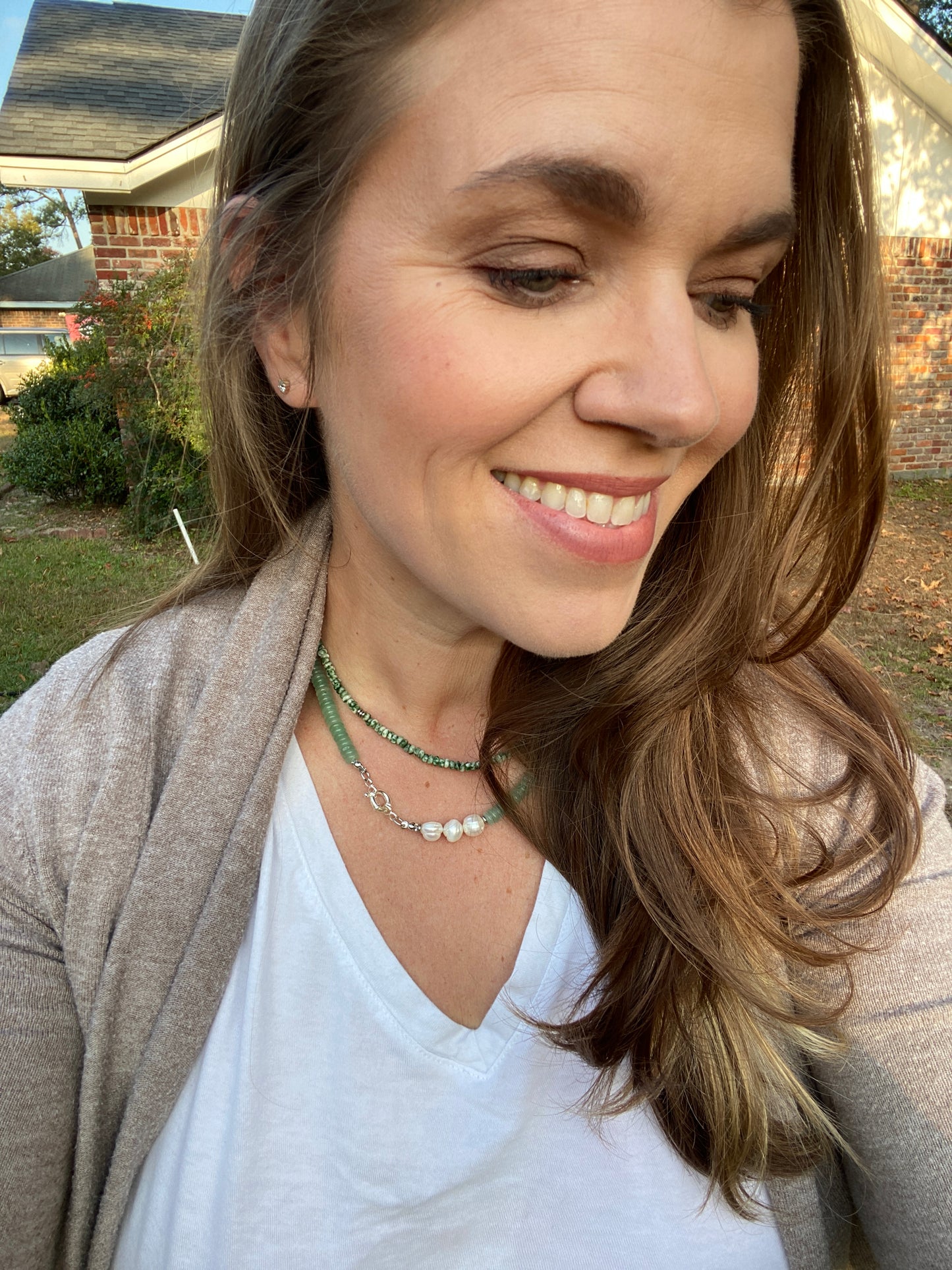 Woman with a smile, wearing a white shirt and beige cardigan, outdoors.