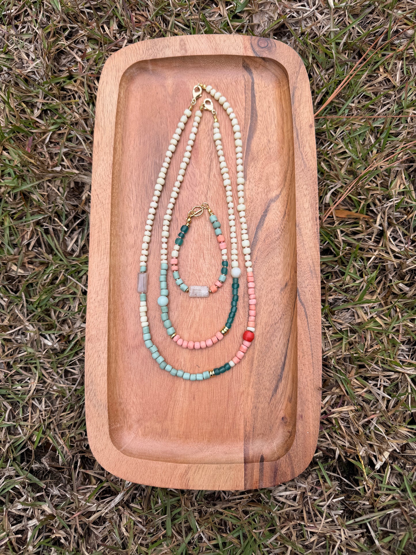Wooden tray with beaded necklaces on a grassy background