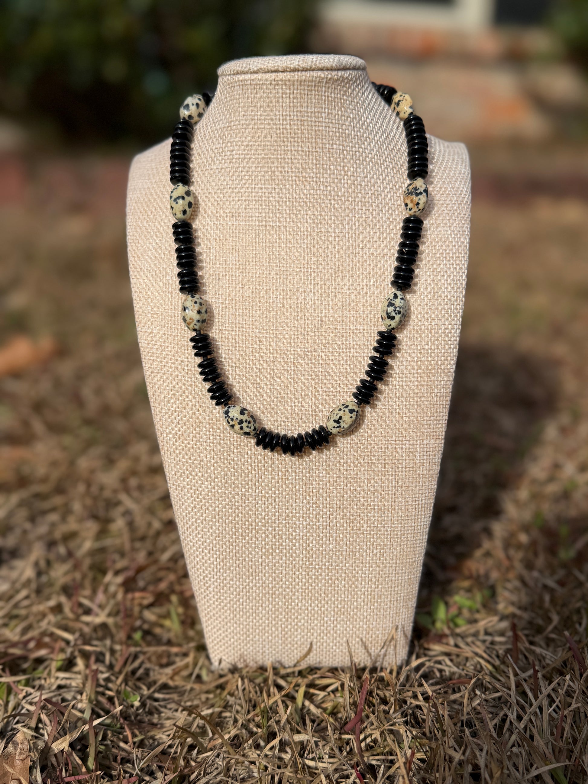 Necklace with black and white beads on a beige bust against a natural background