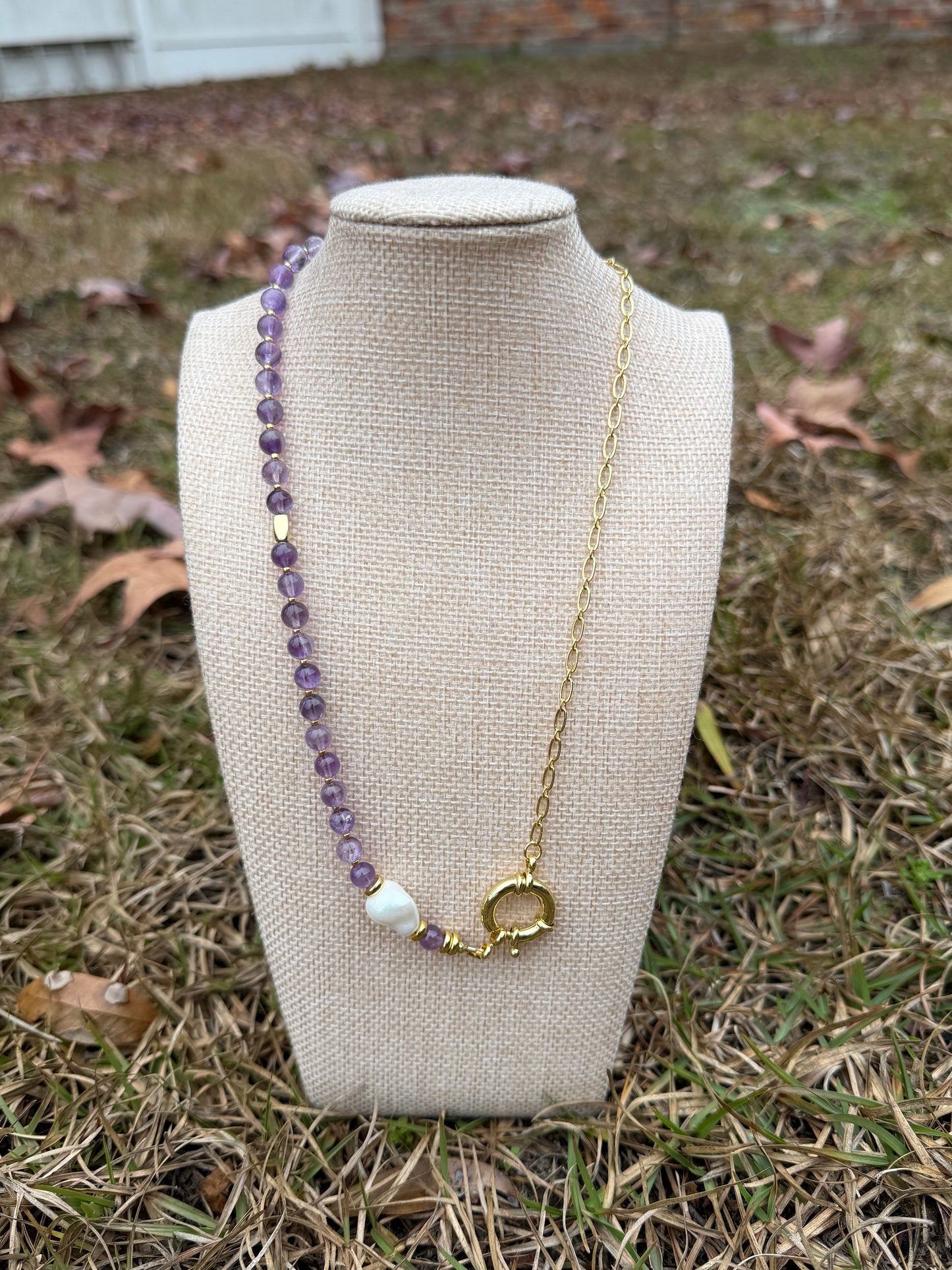 Necklace with amethyst and pearl beads on a beige stand outdoors