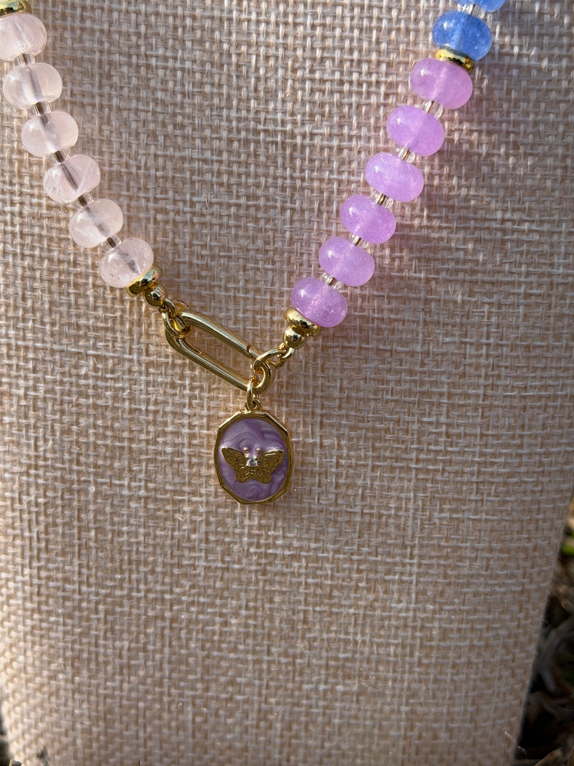 Necklace with purple and clear beads and a gold clasp on a textured fabric background