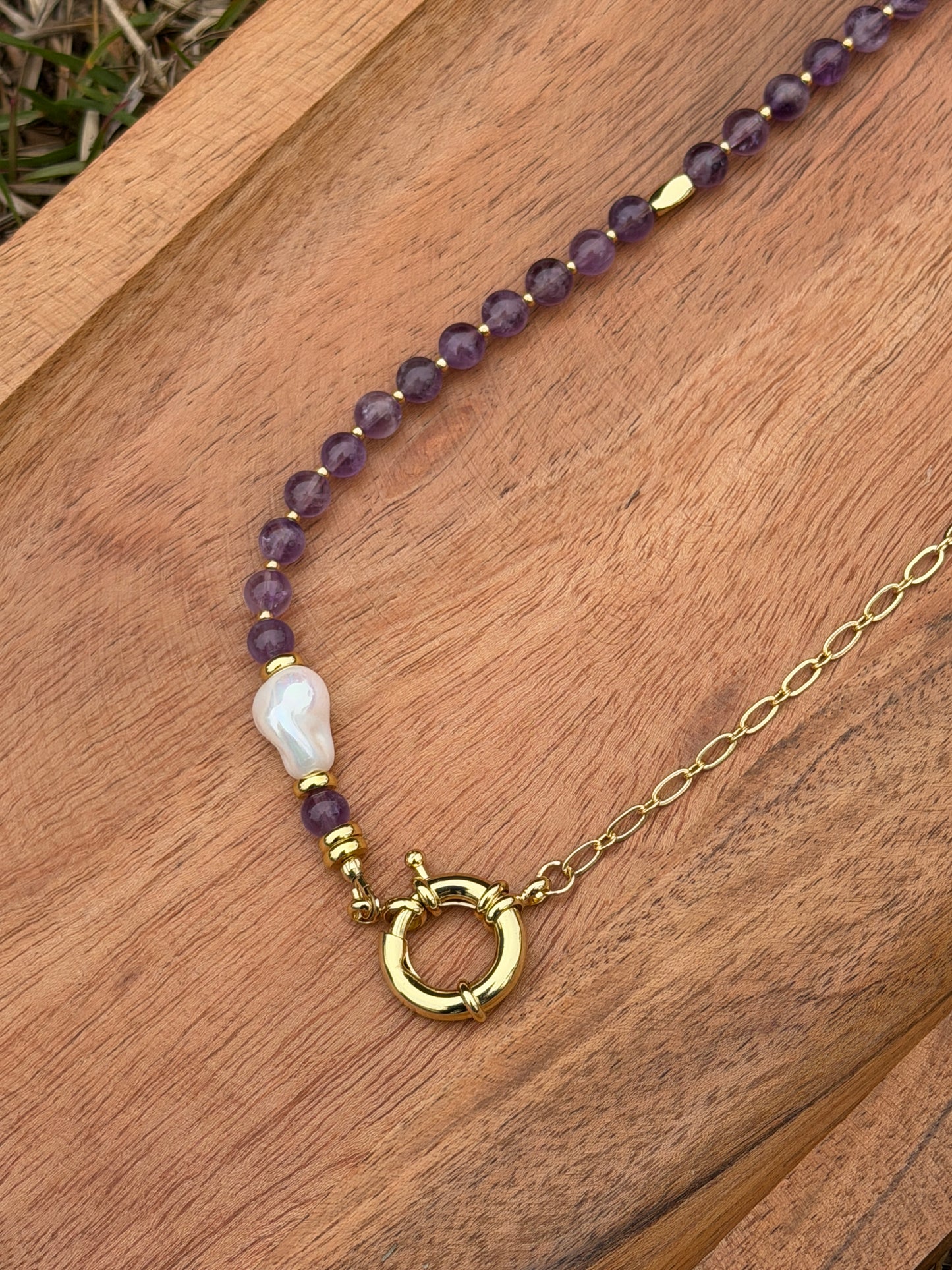 Necklace with amethyst and pearl beads and a gold clasp on a wooden surface