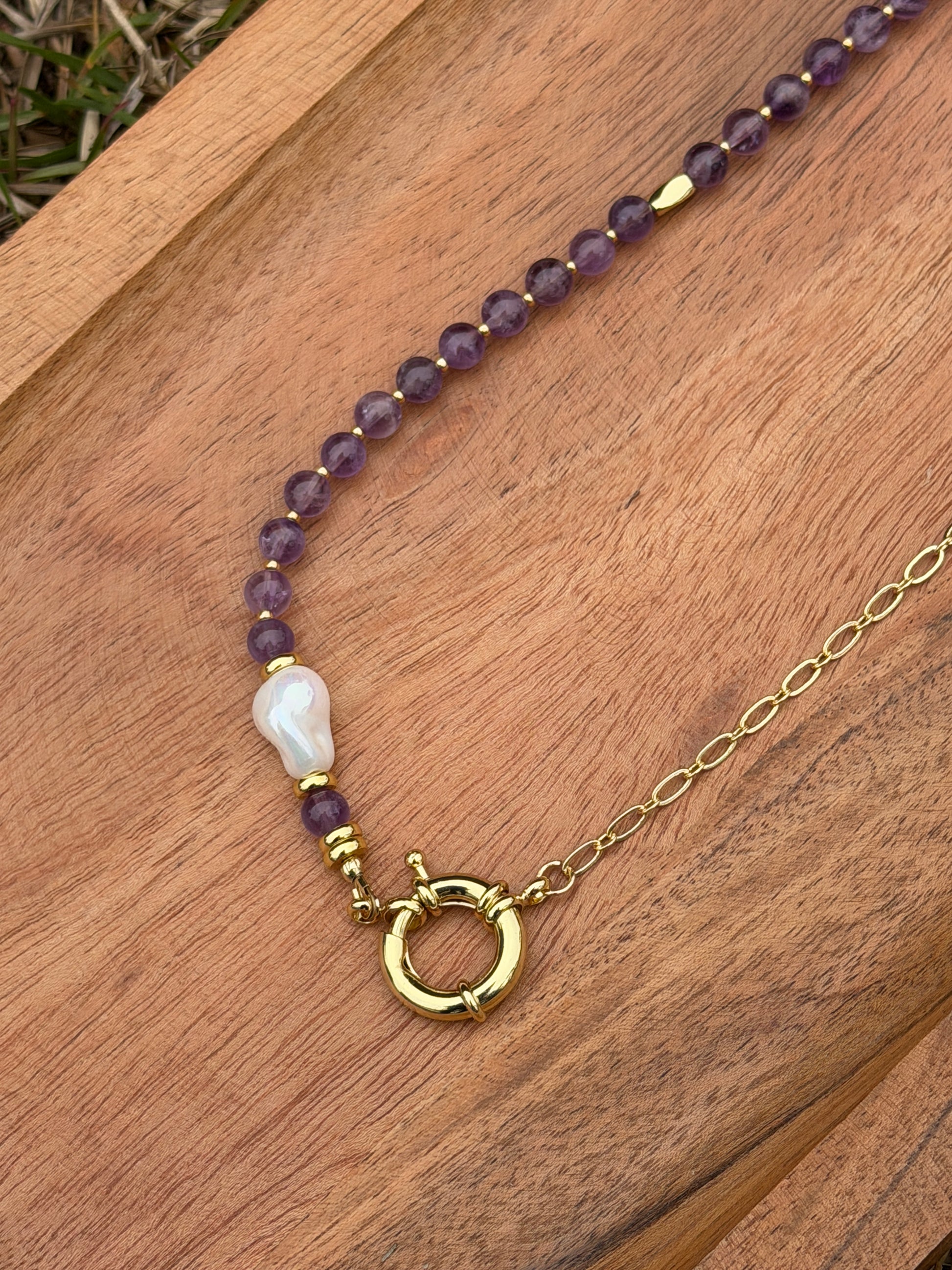Necklace with amethyst and pearl beads and a gold clasp on a wooden surface