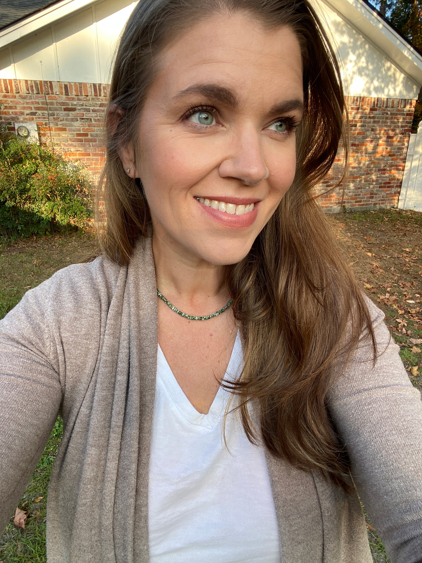 Woman smiling outdoors with a neutral background while wearing green necklace