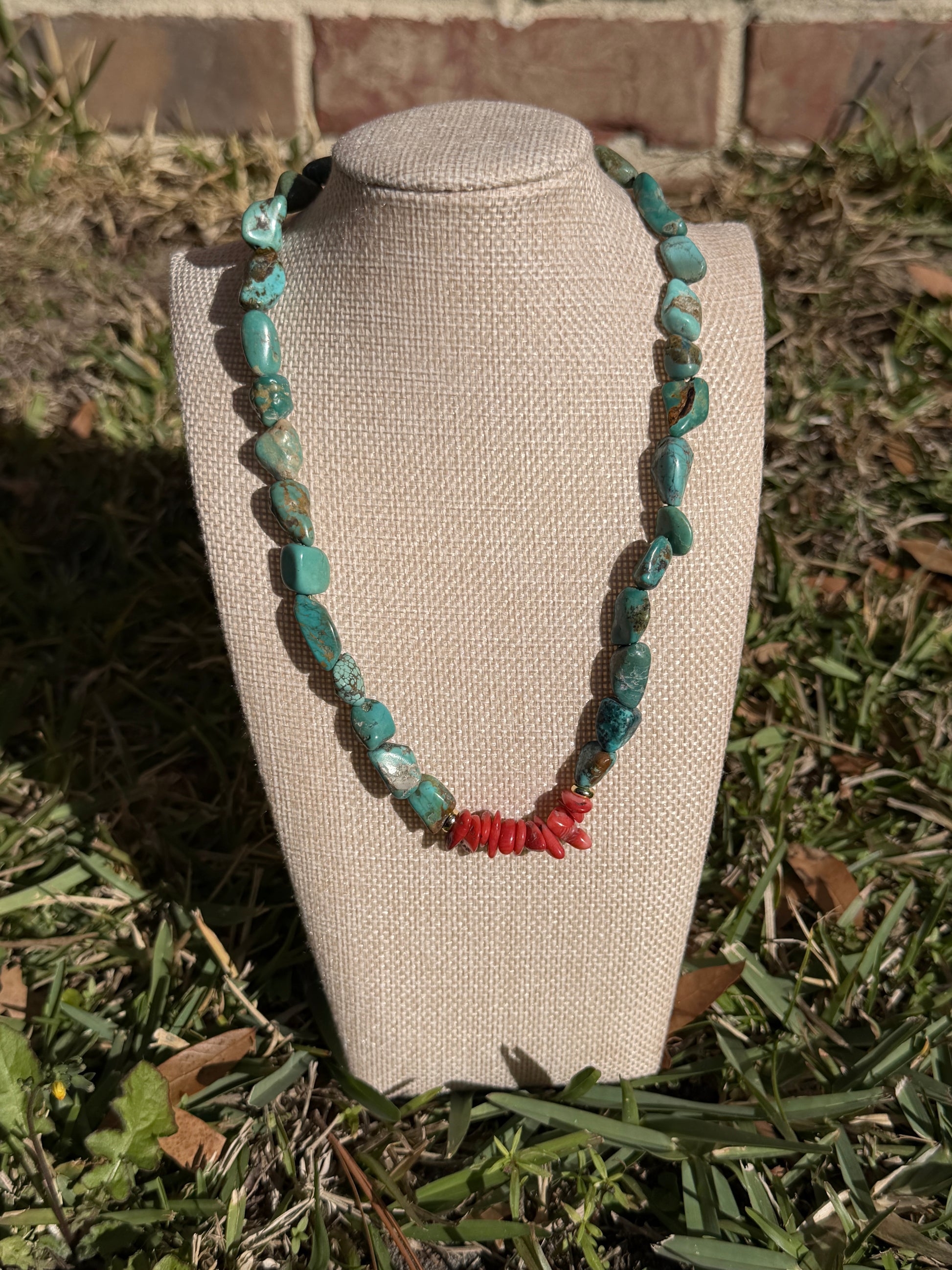 Necklace with turquoise and red beads on a mannequin bust outdoors.