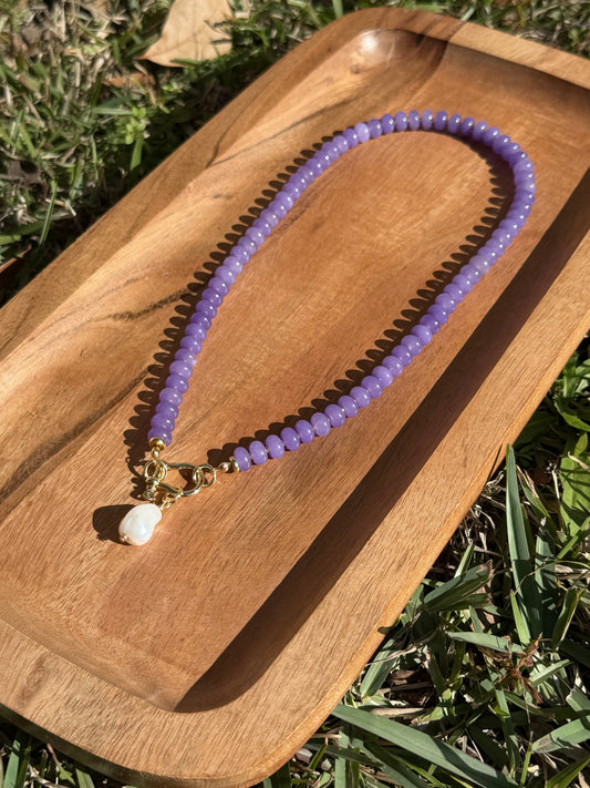 Purple beaded necklace with a pearl pendant on a wooden surface outdoors