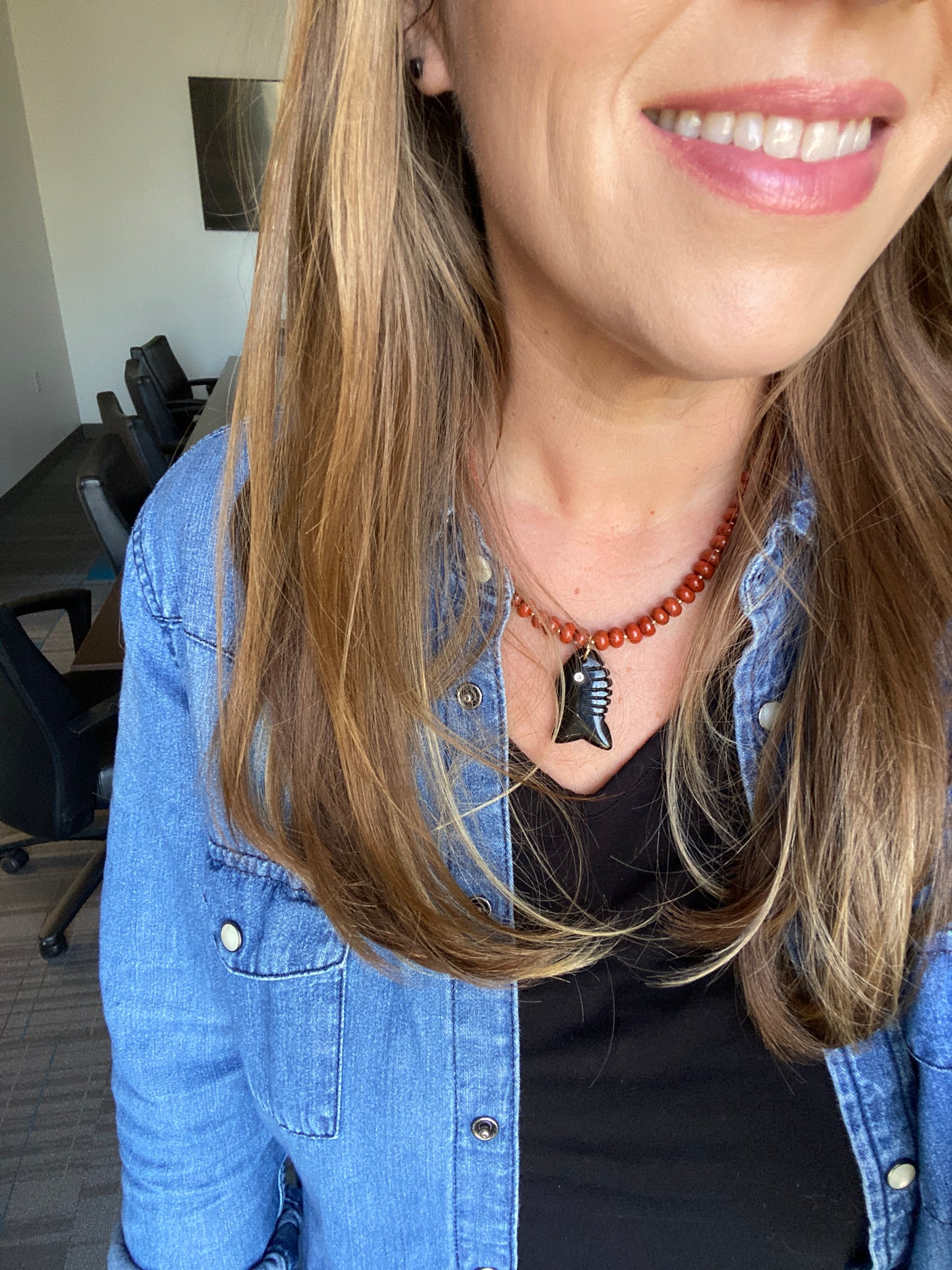 Close-up of a person wearing a red beaded necklace with black fish pendant.
