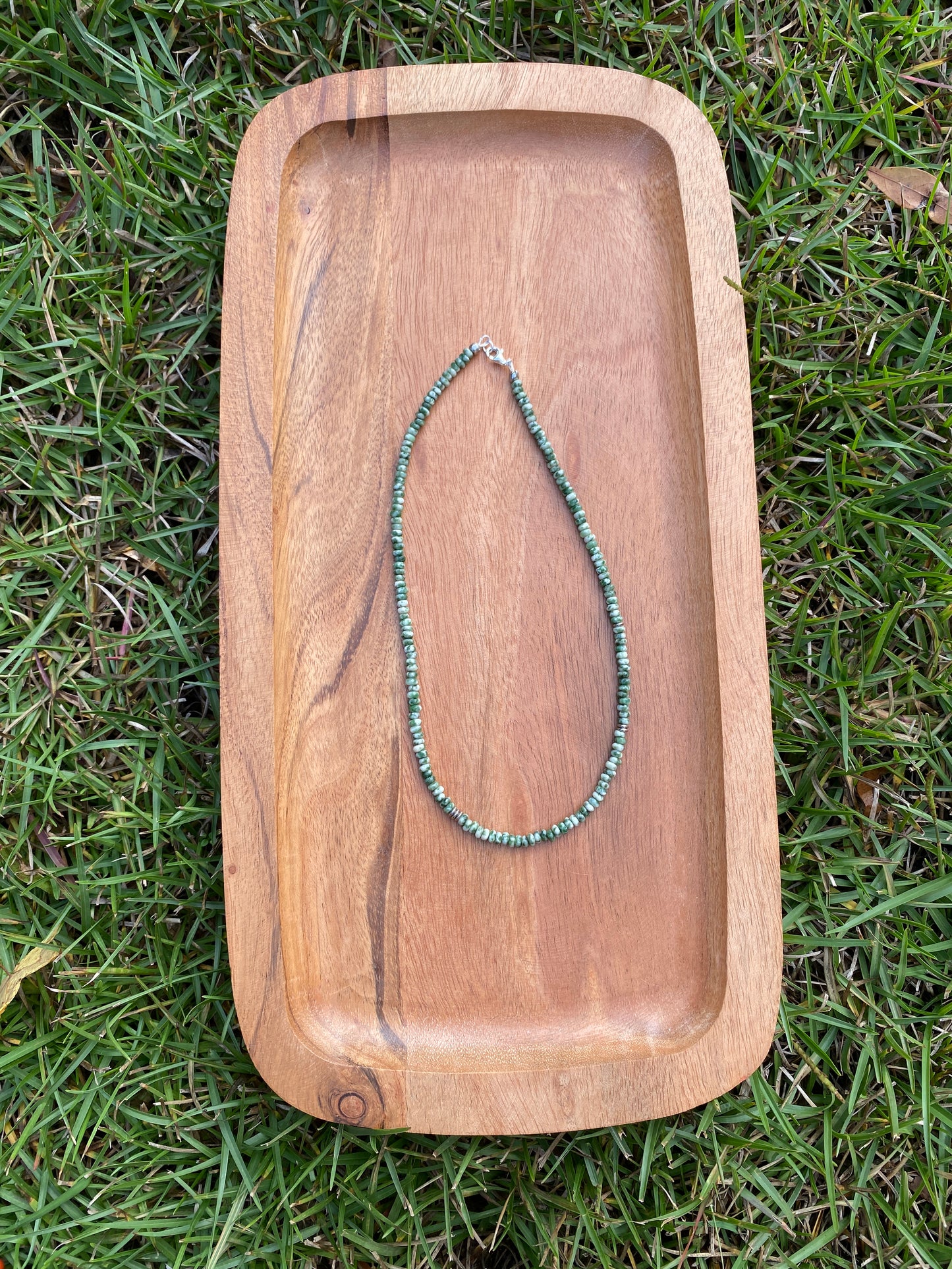 Wooden tray with a green beaded necklace on grass
