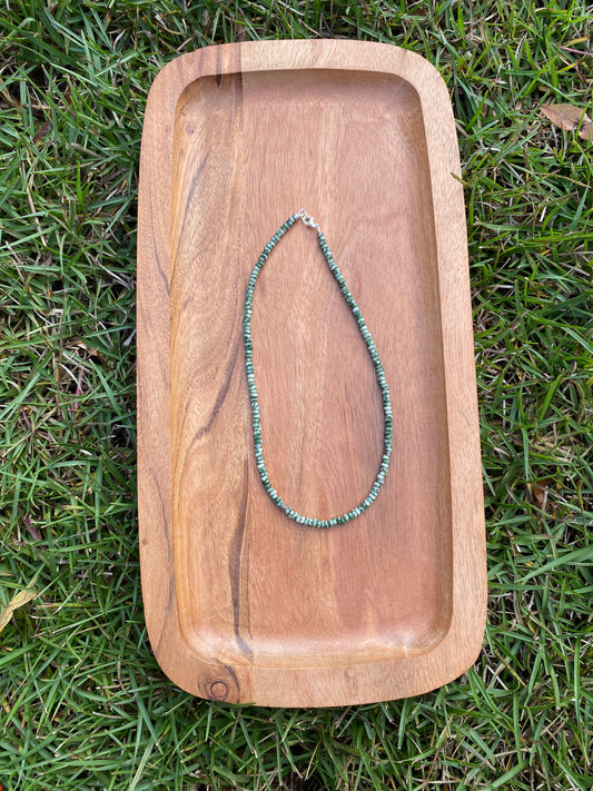 Wooden tray with a green beaded necklace on grass