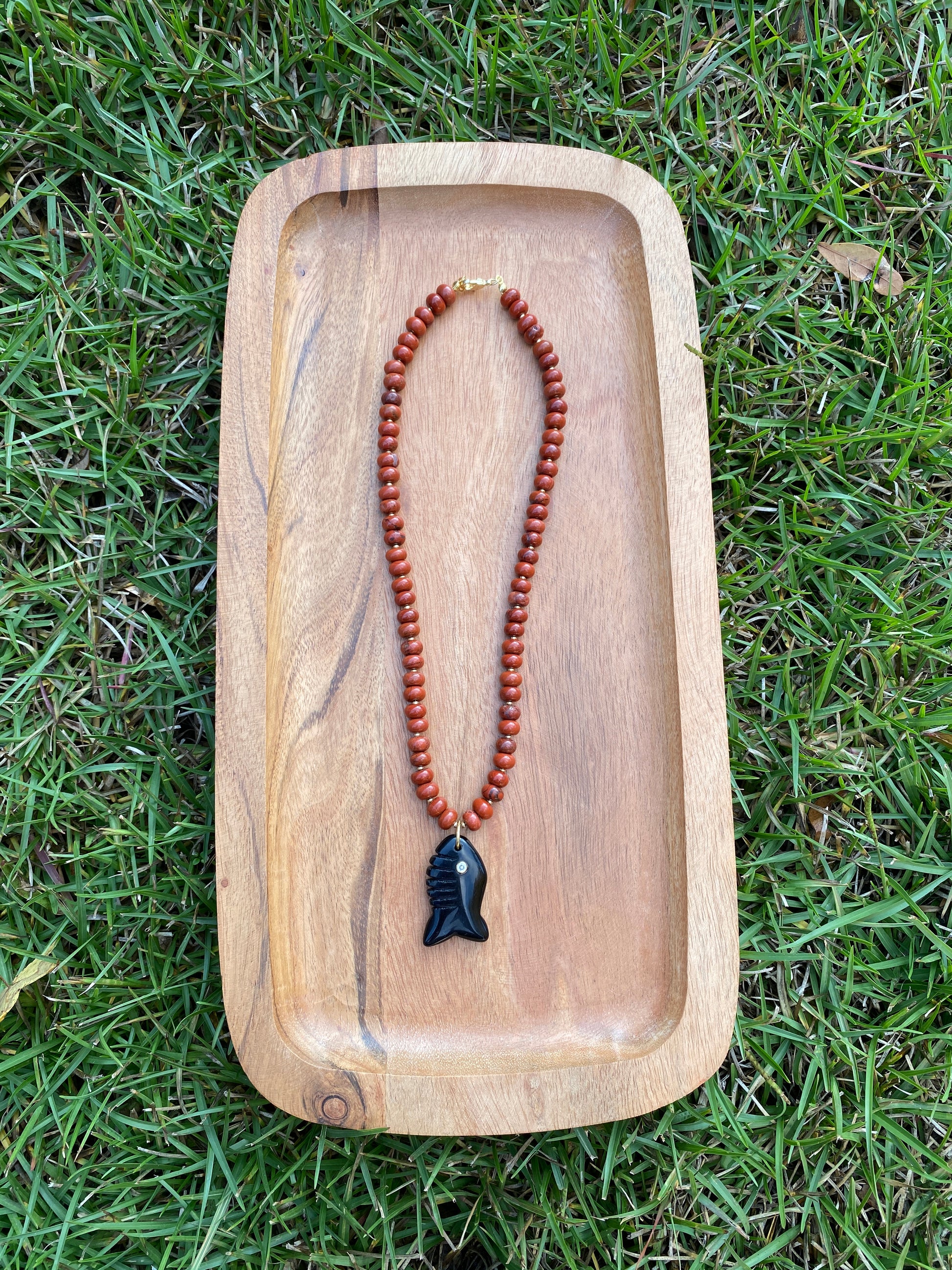 Wooden tray with a red beaded necklace on grass