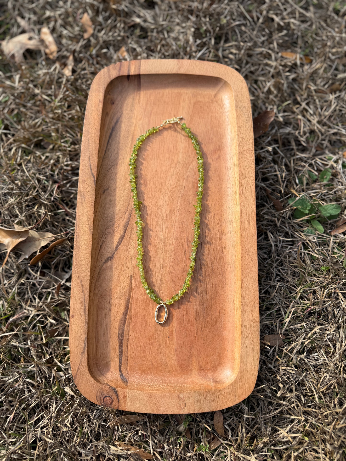 Green necklace on a wooden tray with grass in the background