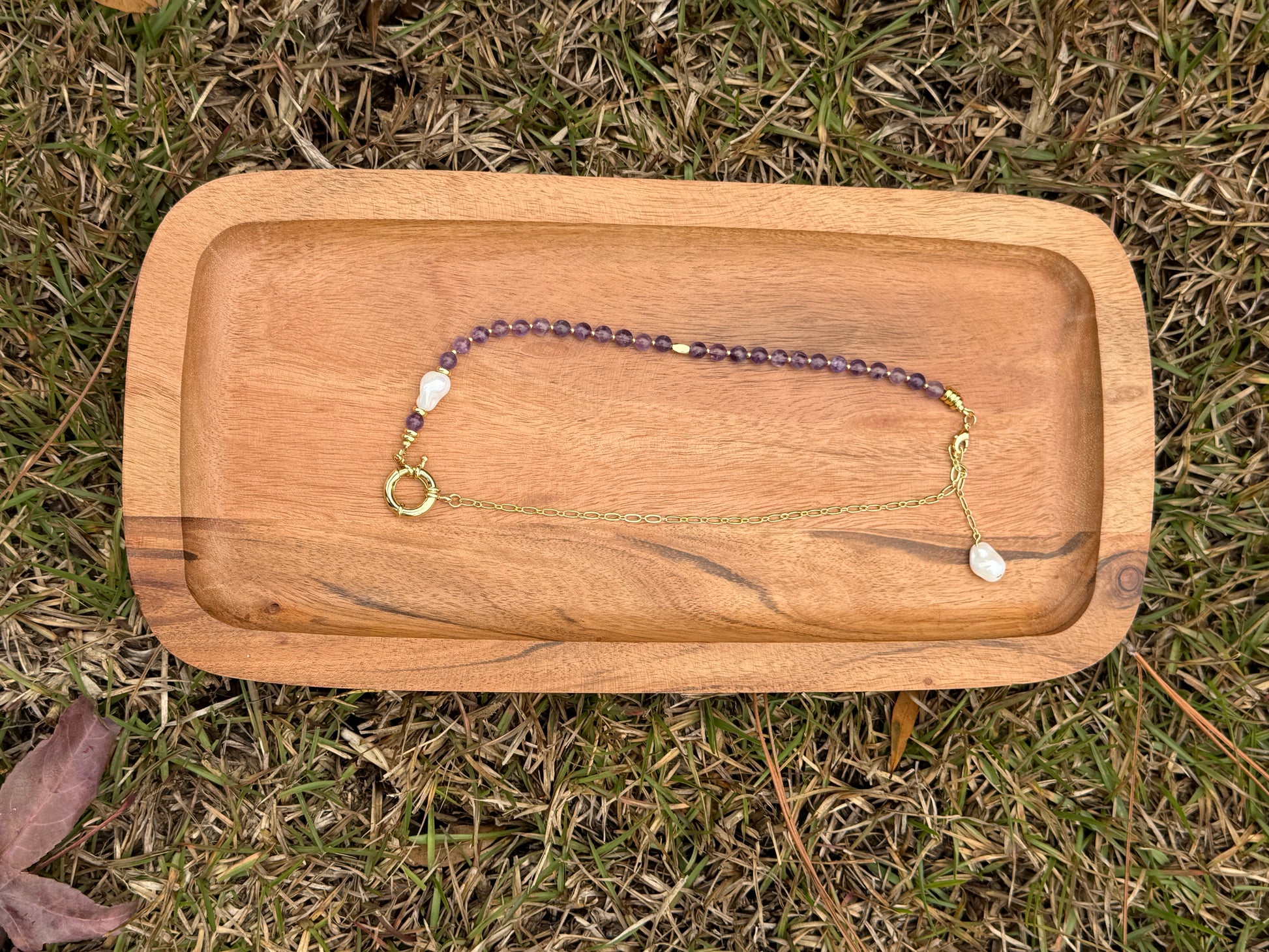 Necklace with amethyst and pearl beads on a wooden tray outdoors