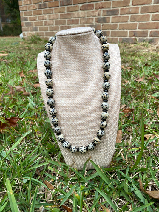 Necklace with black and white beads on a beige cushion outdoors.