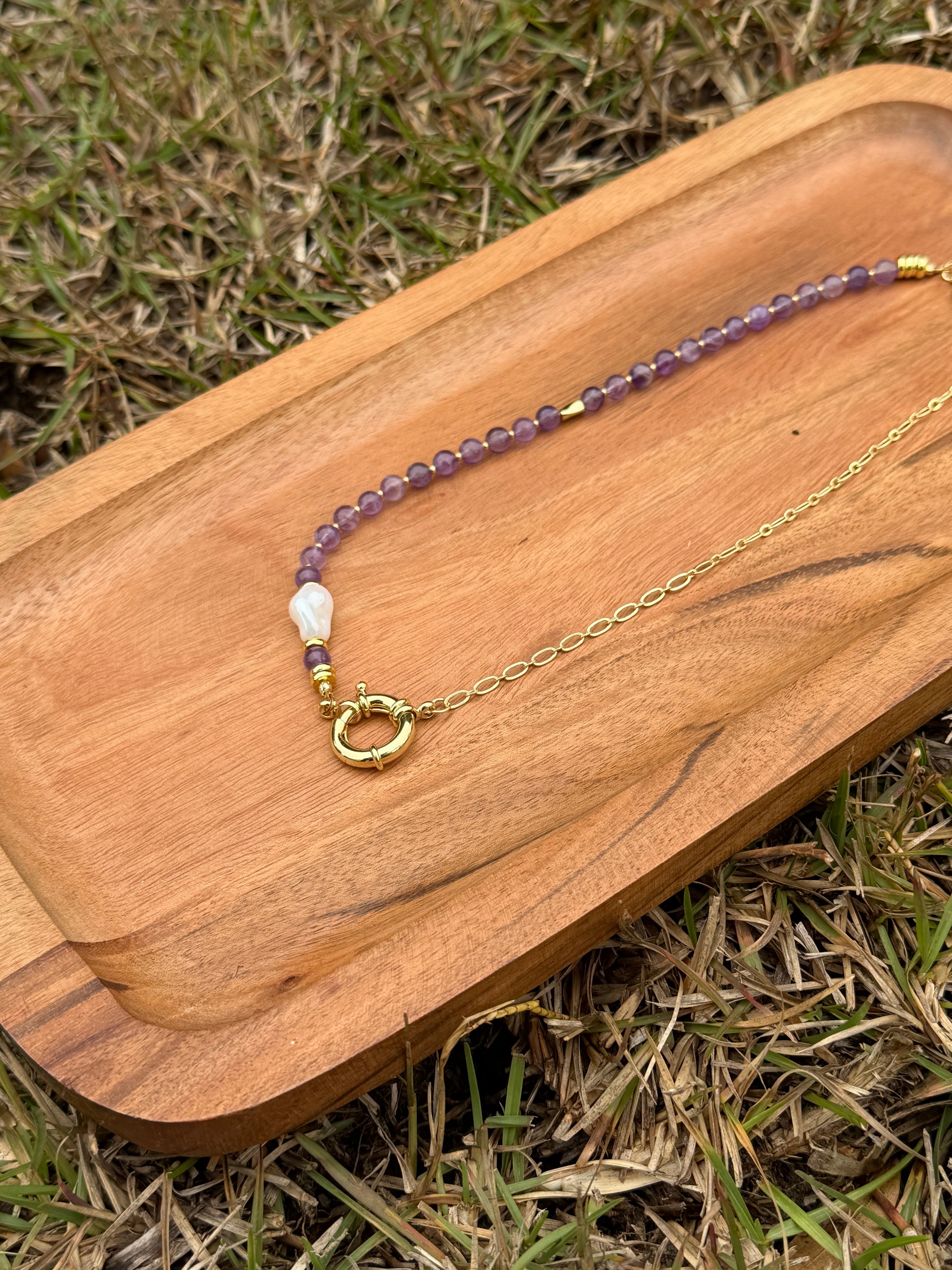 Necklace with amethyst and pearl beads and gold chain on a wooden board outdoors