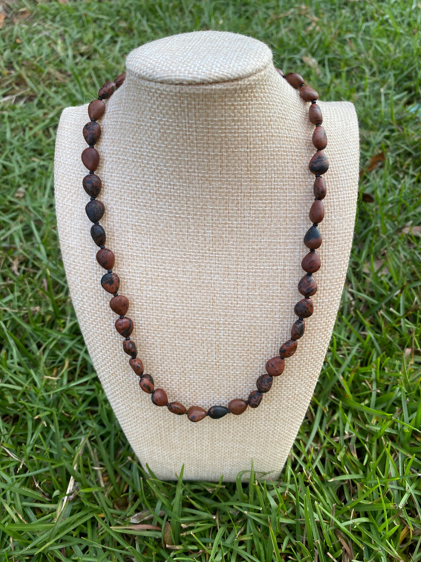 Necklace with brown beads on a beige stand against a grass background