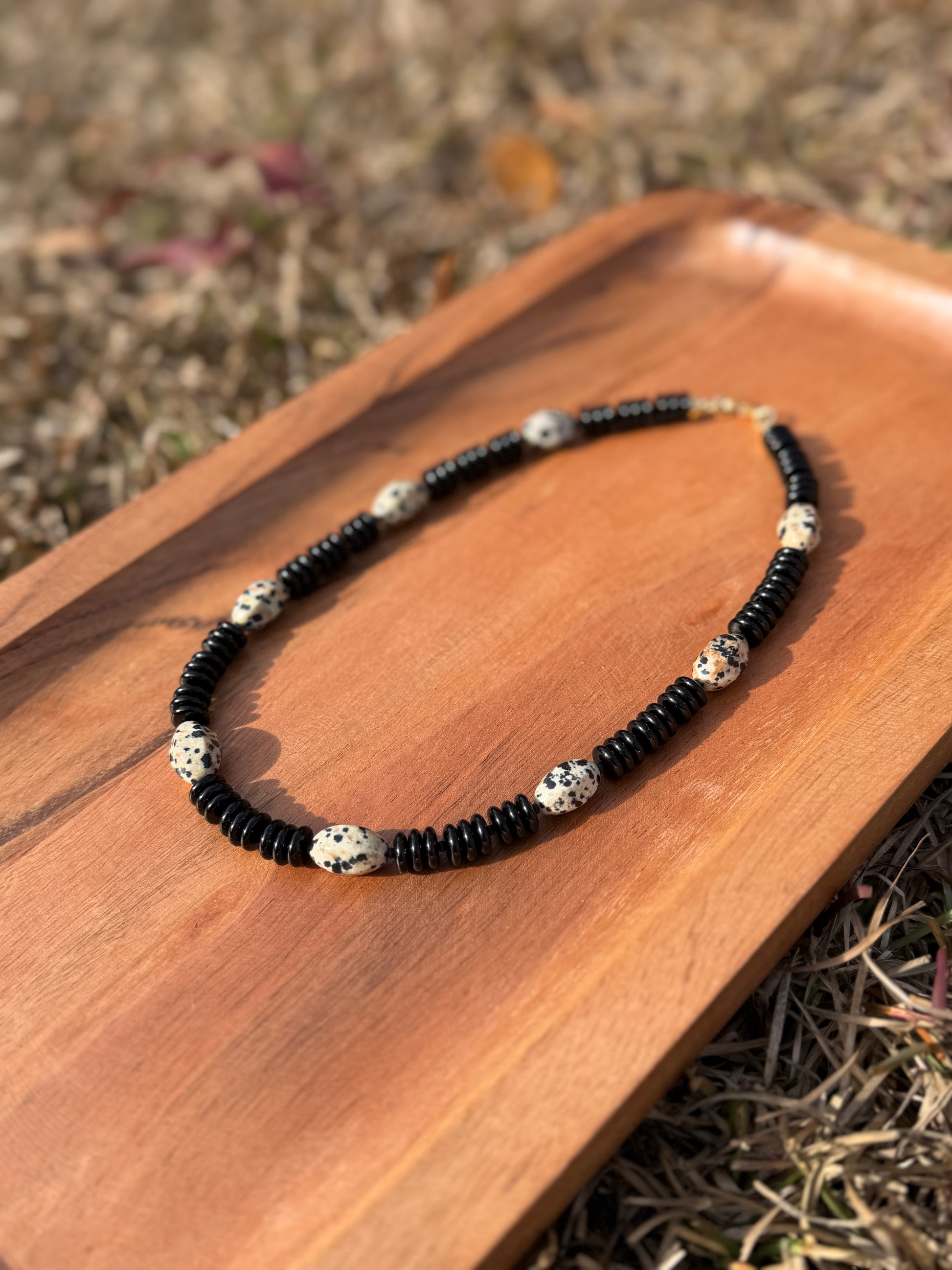 Necklace with black beads and silver accents on a wooden surface