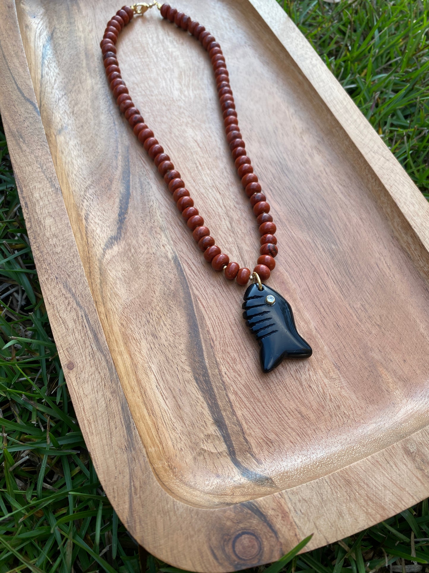 Red beaded necklace with a black fish-shaped pendant on a wooden surface.