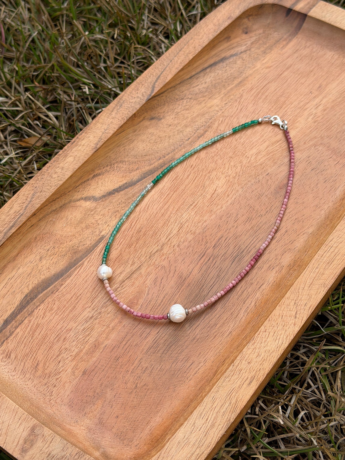 Pink and green necklace with beads on a wooden tray outdoors