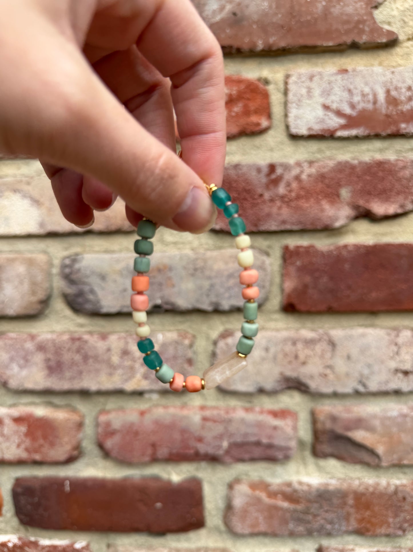 Hand holding a beaded bracelet against a brick wall background