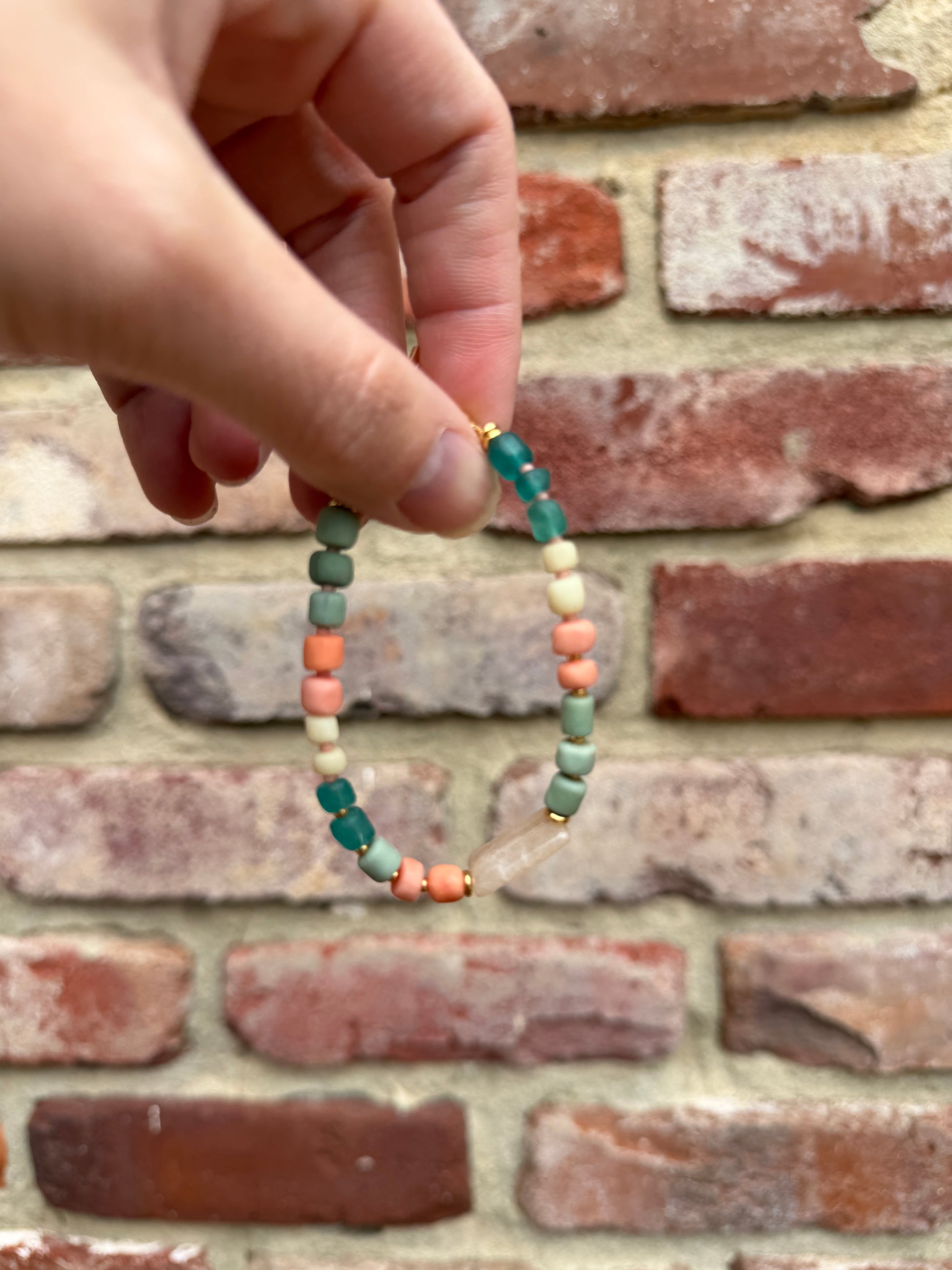 Hand holding a beaded bracelet against a brick wall background