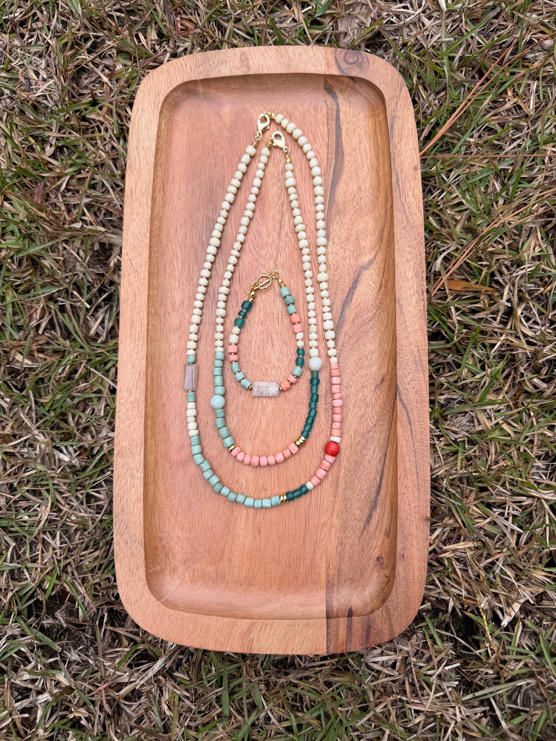 Wooden tray with beaded necklaces on a grassy background